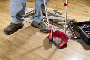 An,Unrecognizable,Contractor,to,fix,water,damage,With,A,Broom,Sweeping,Floor,Into,Dustpan.